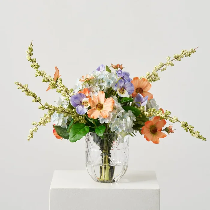 Spring Awakening – Light Blue Hydrangea, Orange Cosmos, Lavender Pansy & Spring Berry Floral Centerpiece Water Illusion Arrangement in Beveled Vase