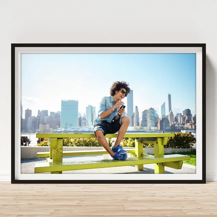 Young Man Using Phone While Sitting On Bench Against Cityscape #1 Art Print